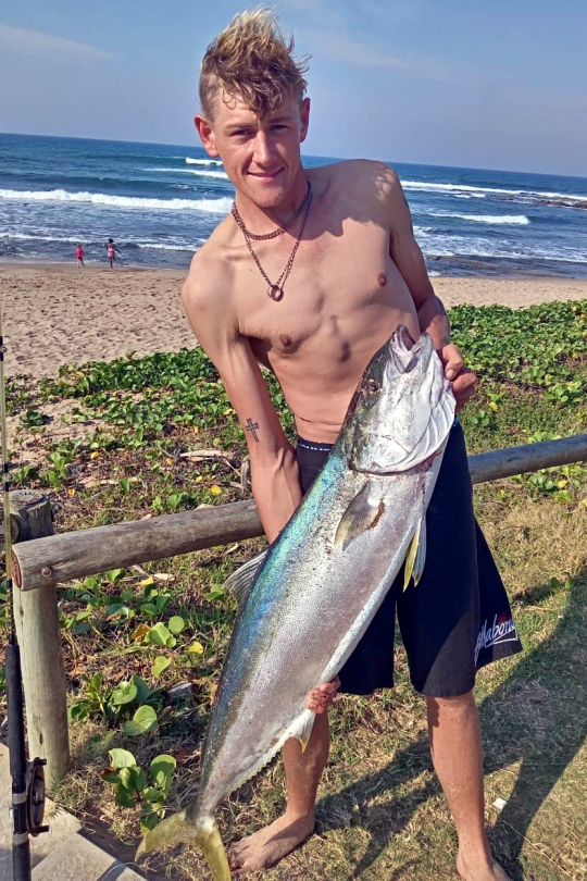 Shirtless angler holding a large silver kingfish catch on the beach, Shelly Beach, South Coast KZN