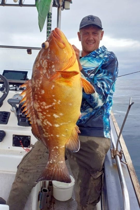 Angler aboard a deep sea charter boat holding a bright orange rockcod caught bottom fishing off Shelly Beach, South Coast KZN