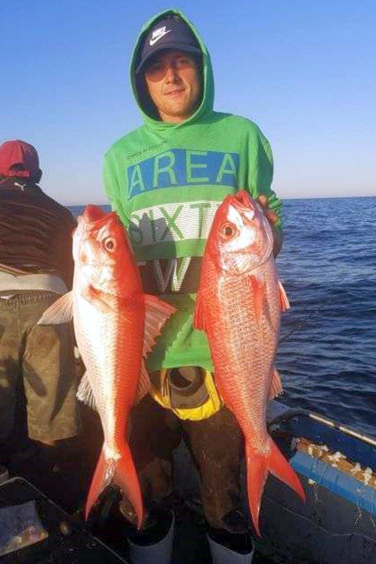 Angler holding two bright red deep-water snapper caught bottom fishing off Shelly Beach, South Coast KZN